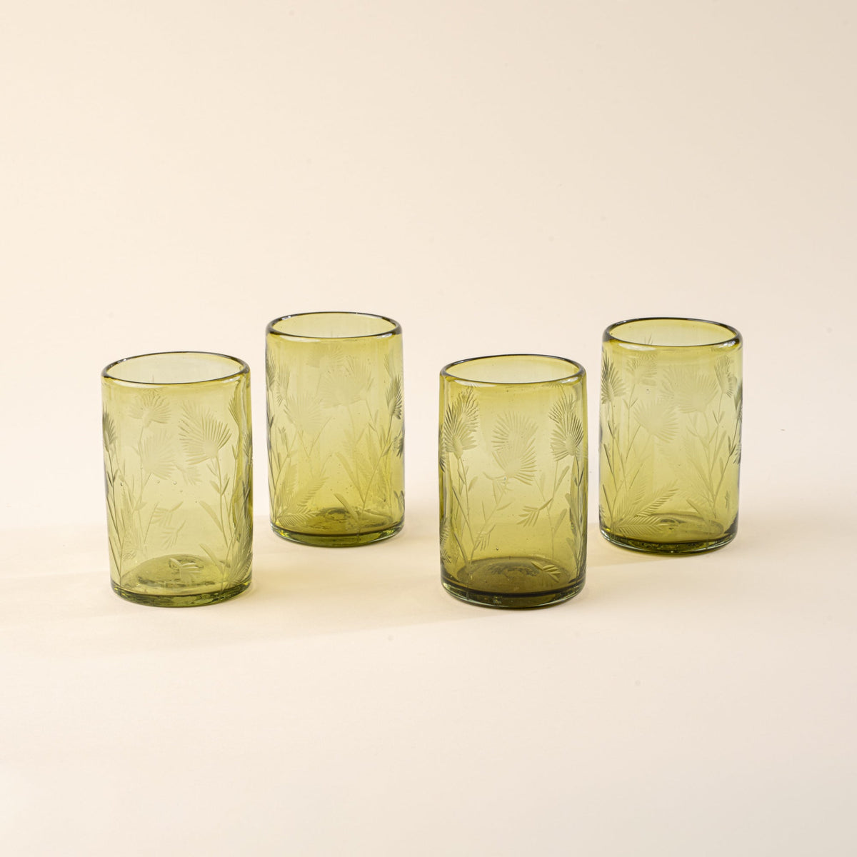 Four olive tumbler glasses made of recycled glass with etched thistle designs on it
